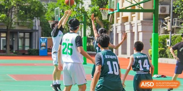 Students in sports uniforms actively playing basketball on an outdoor court at Shanghai Hongqiao International School.