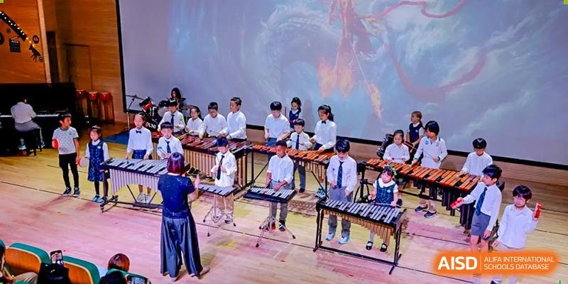 Students performing together in an ensemble, playing marimbas and xylophones on a stage at Shanghai Hongqiao International School.