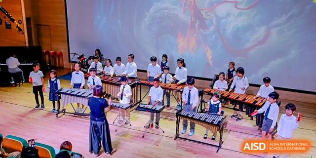 Students performing together in an ensemble, playing marimbas and xylophones on a stage at Shanghai Hongqiao International School.