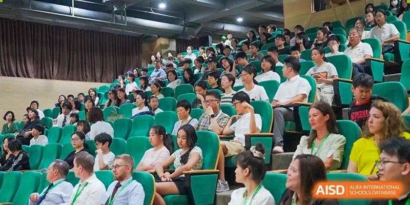 A large group of students and parents seated in a school auditorium or lecture hall, attentively watching a presentation at Shanghai Hongqiao International School.