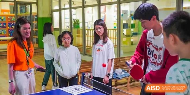 Two students watching a table tennis (ping pong) game indoors at Shanghai Hongqiao International School.