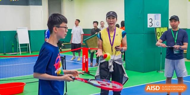A teacher or student in a yellow vest demonstrating a shot during an indoor racket sport activity at Shanghai Hongqiao International School.