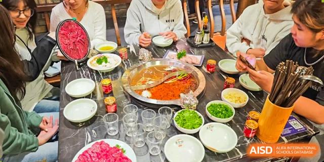 Students or staff enjoying a shared meal with various dishes, including a whole fish, on a table at Shanghai Hongqiao International School.