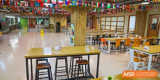 A bright dining or common area with wooden tables and chairs, decorated with international flags at Shanghai Hongqiao International School.