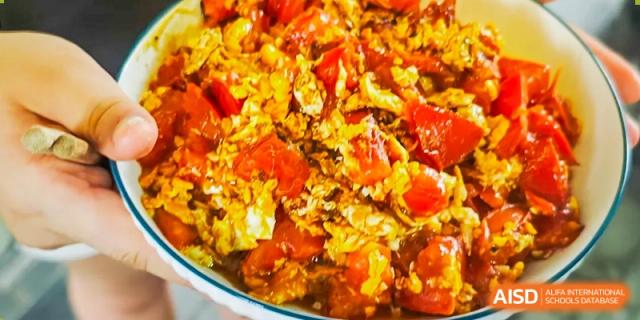 A close-up photo of a prepared stir-fried dish featuring eggs and tomatoes at Shanghai Hongqiao International School.