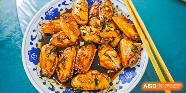 A close-up photo of a plate of cooked, glazed chicken wings at Shanghai Hongqiao International School.