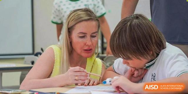 A female teacher providing focused assistance to a young student during a classroom activity at Shanghai Hongqiao International School.