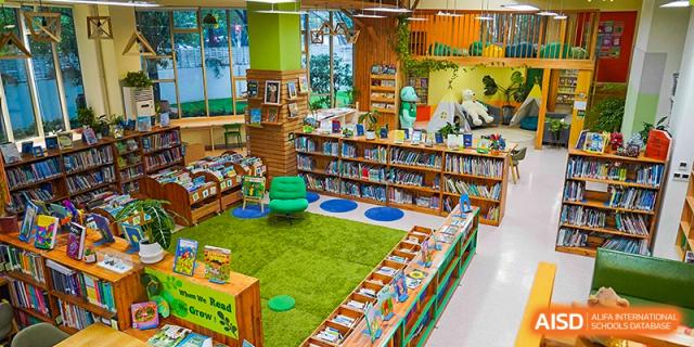 A wide, inviting shot of a colorful and well-stocked school library with a green carpet reading area and wooden shelves at Shanghai Hongqiao International School.
