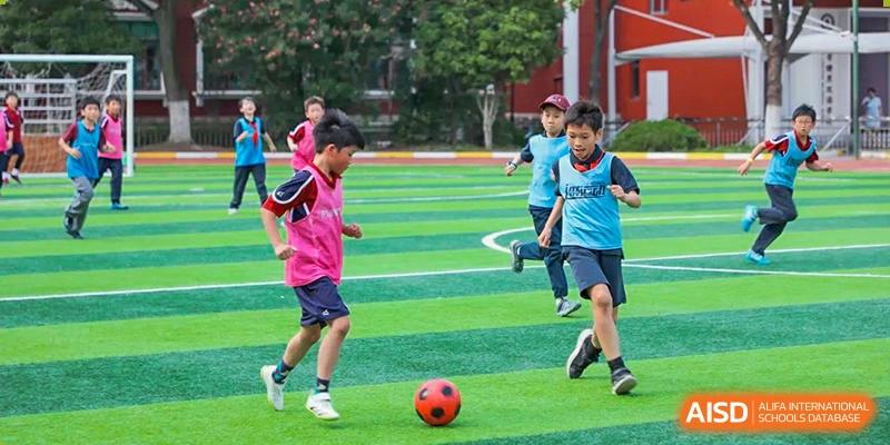A group of students playing soccer on a green sports field during an outdoor physical education class at Shanghai Liaoyuan Bilingual School.
