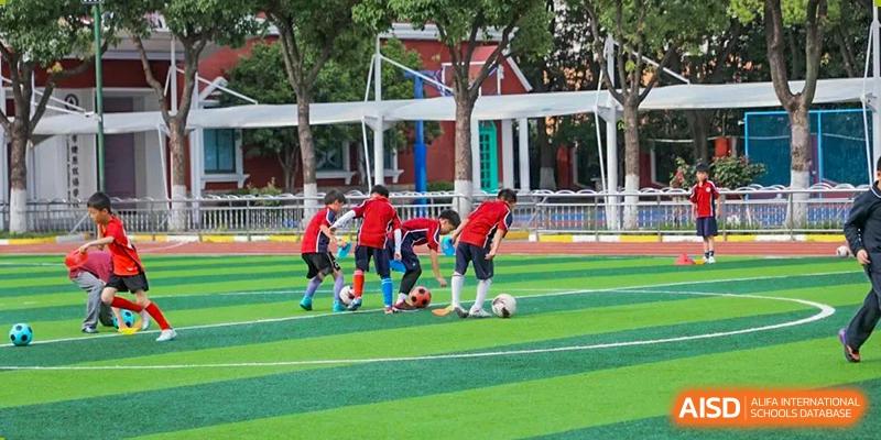 Several young students practicing soccer drills with balls on the striped green sports field at Shanghai Liaoyuan Bilingual School.