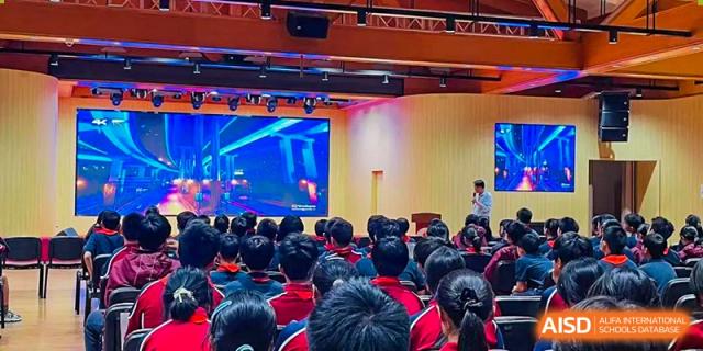 A large group of students in red shirts seated in an auditorium, watching a presentation or performance on a large screen at Shanghai Liaoyuan Bilingual School.