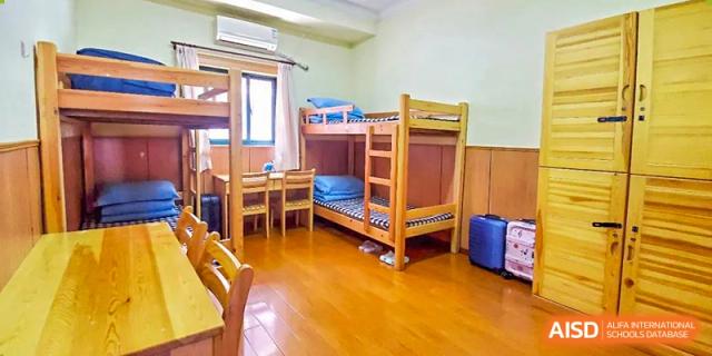 A clean and furnished dormitory room at Shanghai Liaoyuan Bilingual School featuring wooden bunk beds, desks, and wood flooring.