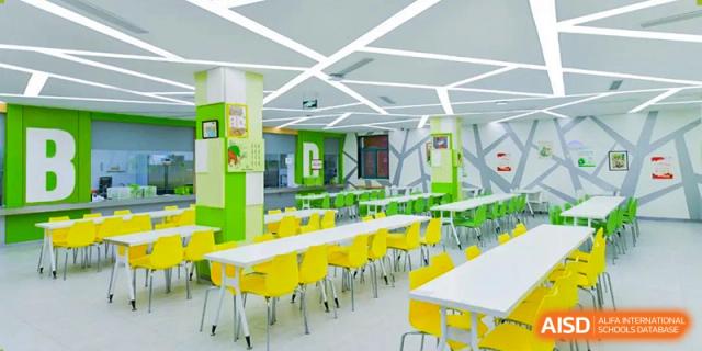 The modern and brightly colored cafeteria at Shanghai Liaoyuan Bilingual School, featuring lime green walls and rows of yellow and white dining tables and chairs.