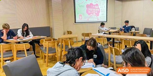 QSI International School of Shenzhen students collaborating closely on schoolwork at a small wooden table in a brightly lit learning area.