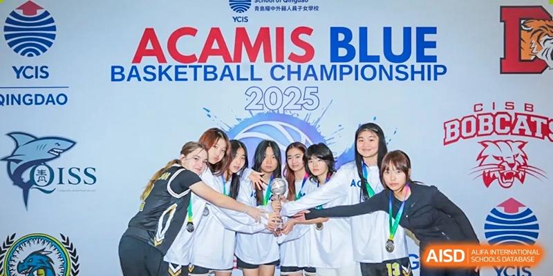 The QSI International School of Shenzhen Girls' Basketball team celebrating their CAMIS BLU Basketball Championship 2025 victory, holding a trophy under a banner.