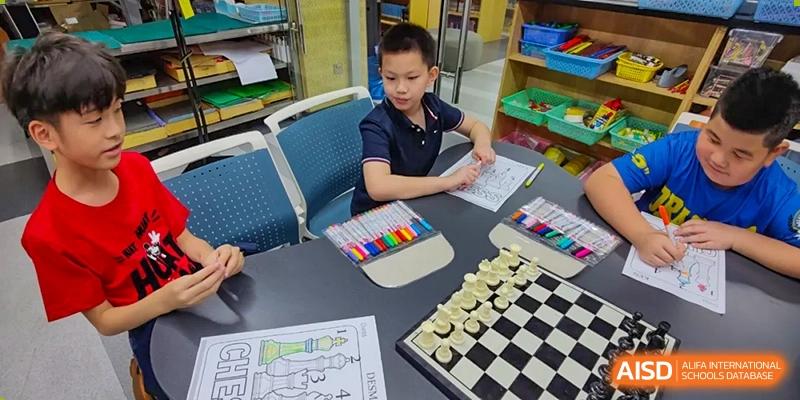 A close-up of a table where QSI International School of Shenzhen students are engaged in activities, showing a chessboard and art supplies like markers.