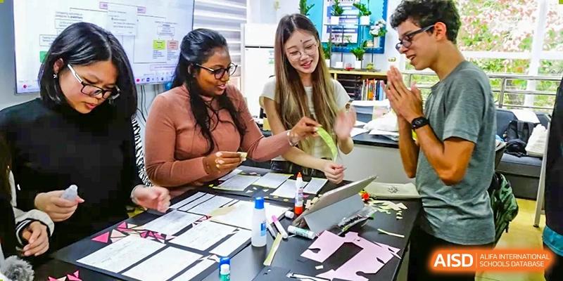 QSI International School of Shenzhen students collaborating on a hands-on art or design project using scissors, glue, and paper.