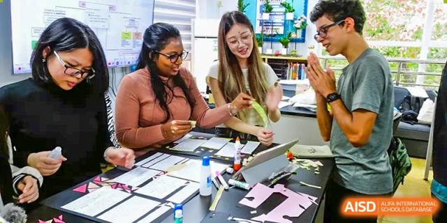 QSI International School of Shenzhen students collaborating on a hands-on art or design project using scissors, glue, and paper.