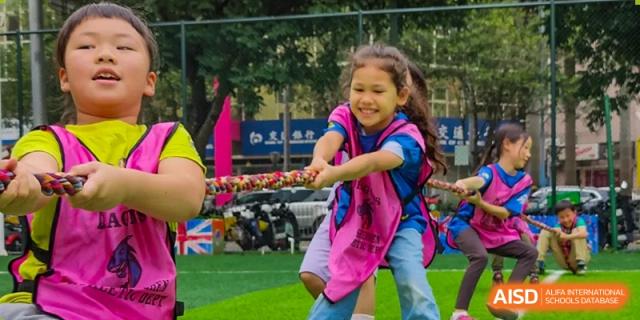 A smiling young female student from QSI International School of Shenzhen participating intensely in a game of tug-of-war.