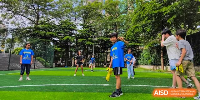 A young student from QSI International School of Shenzhen participating in an outdoor game or activity on a green field.