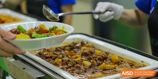 A close-up of a buffet tray containing a richly flavored meat dish (like beef stew or curry) offered at QSI International School of Shenzhen.