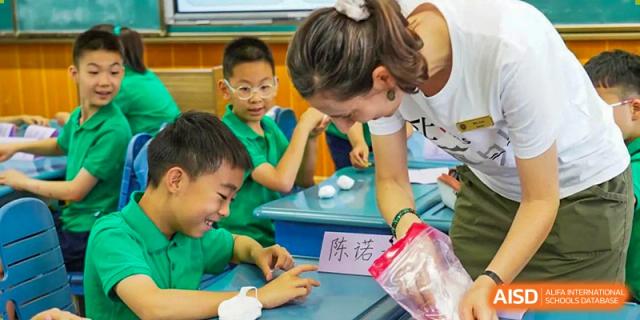 A female teacher assisting two young boys with a hands-on learning activity at a table at Suzhou Foreign Language School.