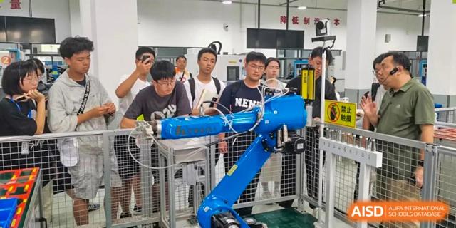 Students observing and interacting with a blue robotic arm in a technical or engineering workshop at Suzhou Foreign Language School.