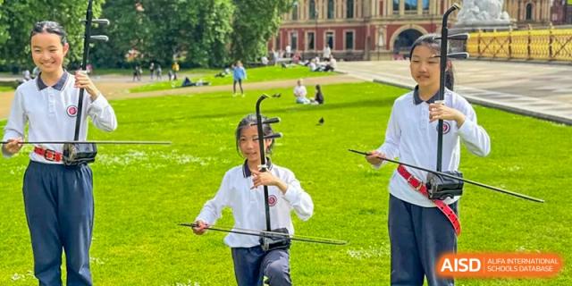 Student playing the erhu, a traditional Chinese instrument, outdoors on the grass with an instructor at Suzhou Foreign Language School.