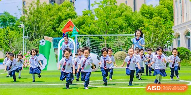 Group of cheerful young students running across a green sports field during an outdoor activity at Suzhou Foreign Language School.