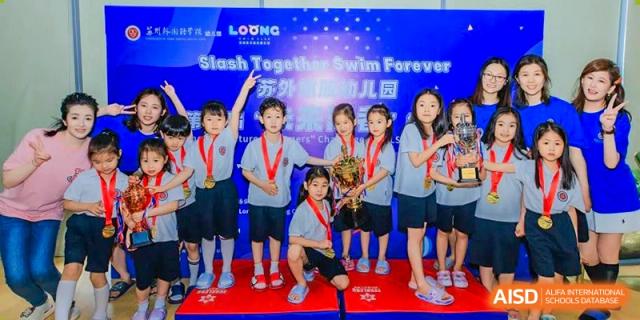 Students posing on a podium with medals and a banner after a swimming competition ("Splash Together Swim Forever") at Suzhou Foreign Language School.