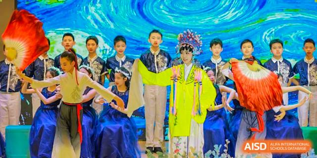 A group of students on stage in colorful traditional costumes, including Chinese opera attire, posing for a photo at Suzhou Foreign Language School.