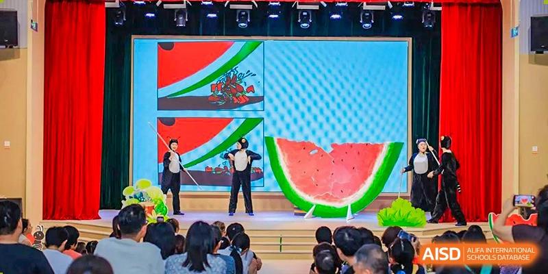 A student giving a presentation or performing with large watermelon graphics on a screen in the background at Suzhou Foreign Language School.