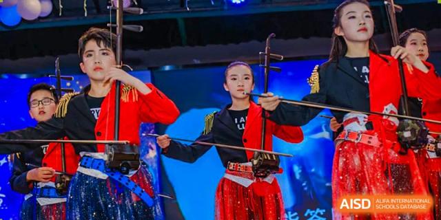 A student in a red and black performance outfit playing the erhu, a traditional Chinese two-stringed fiddle, on stage at Suzhou Foreign Language School.
