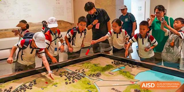 Students gathered around an educational display or terrain model, learning with a teacher at Suzhou Foreign Language School.