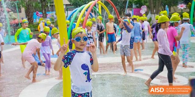 A young boy in sunglasses and a colorful shirt enjoying a water spray park activity with other students at Suzhou Foreign Language School.