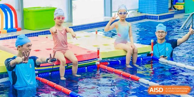 Two young students sitting by the edge of a pool, wearing swim caps and goggles, during a break from swimming activities at Suzhou Foreign Language School.