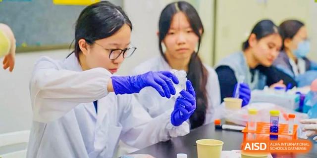 Students in lab coats and blue gloves attentively watching a demonstration of a science procedure in a laboratory setting at Tianjin Farragut School.