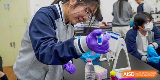 A female student wearing safety goggles and purple gloves, precisely measuring a liquid during a chemistry or science experiment at Tianjin Farragut School.