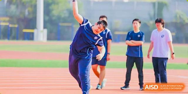 A student in a blue uniform throwing a shot put or practicing a similar track and field event on the running track at Tianjin Farragut School.