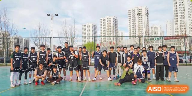 A large group of students in dark sports uniforms posing for a team photo on an outdoor court with city buildings in the background at Tianjin Farragut School.