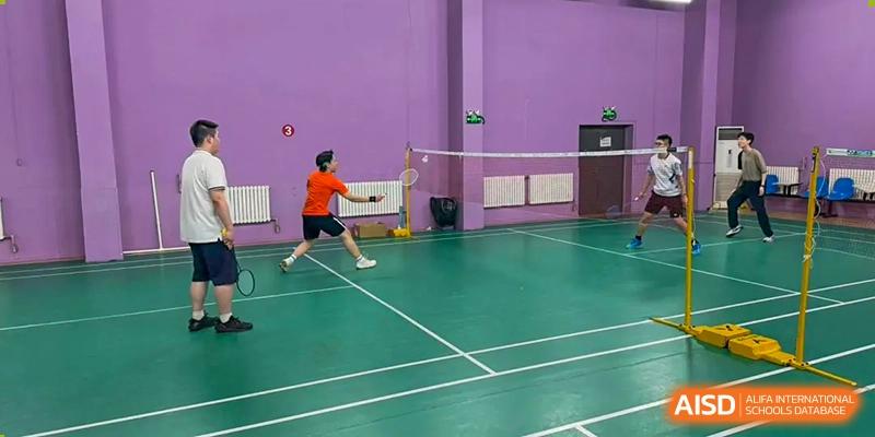 Two students playing badminton on an indoor court with green flooring and purple walls at Tianjin Farragut School.