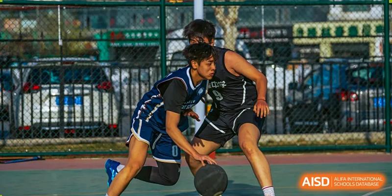Two students aggressively contesting the ball during a basketball game played outdoors at Tianjin Farragut School.