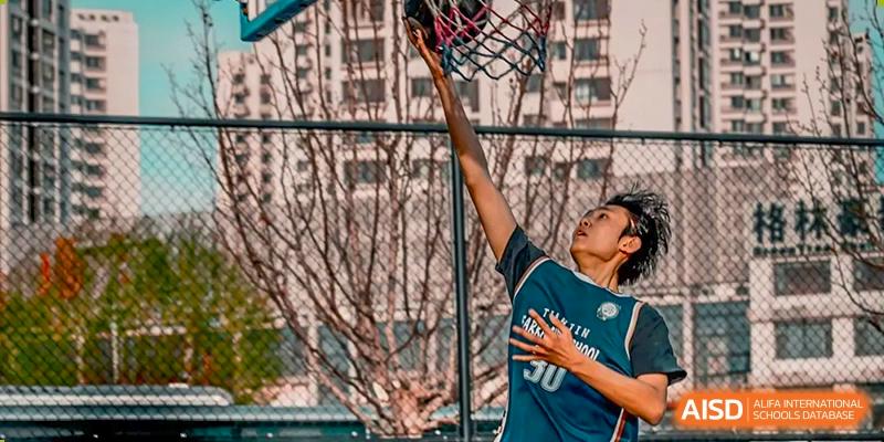 A student in a blue jersey shooting a basketball towards the hoop during a practice or game at Tianjin Farragut School.