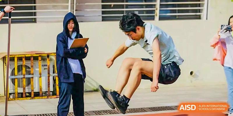 A student jumping during a long jump or agility exercise while a peer records data on a tablet during a physical education class at Tianjin Farragut School.