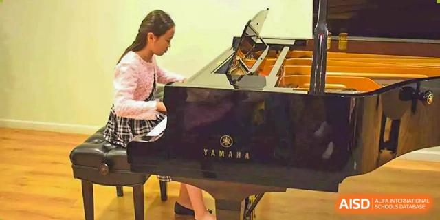 A close-up of a student playing a black Yamaha grand piano during a music performance or lesson at Tianjin Farragut School.
