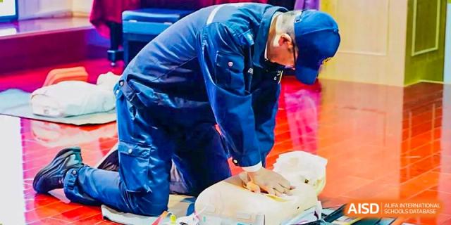 An adult instructor in blue uniform demonstrating Cardiopulmonary Resuscitation (CPR) on a training dummy during a health and safety class at Tianjin Farragut School.