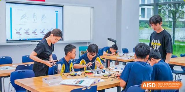 A group of male students in uniform are focused on building and wiring electronic projects at desks in a dedicated workshop space at Ardingly College Zhongshan (ACZS), promoting engineering skills.