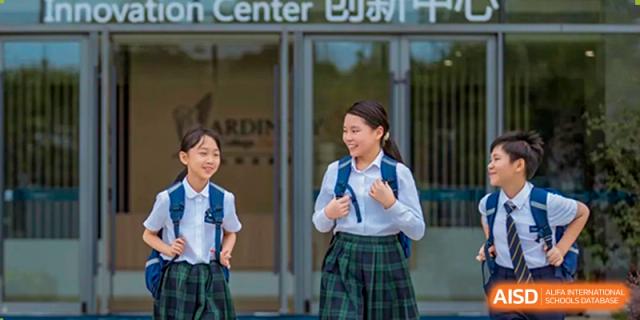 Two cheerful female students in their distinctive school uniforms with plaid skirts and backpacks are walking and talking outside the entrance of Ardingly College Zhongshan (ACZS).