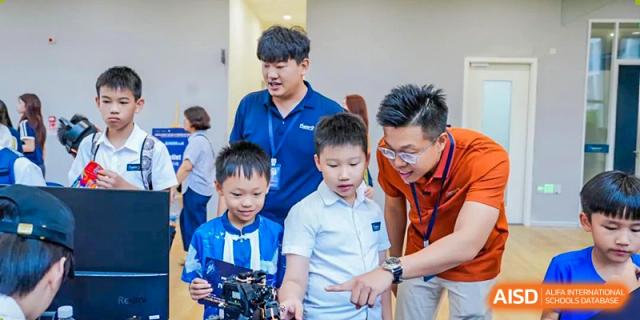 Older students or mentors are guiding young children with a hands-on technical project or robotics demonstration at Ardingly College Zhongshan (ACZS), emphasizing mentorship and peer teaching.