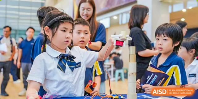 A young female student is carefully holding and examining a small drone or technical device with guidance from an adult at Ardingly College Zhongshan (ACZS), promoting early years tech engagement.